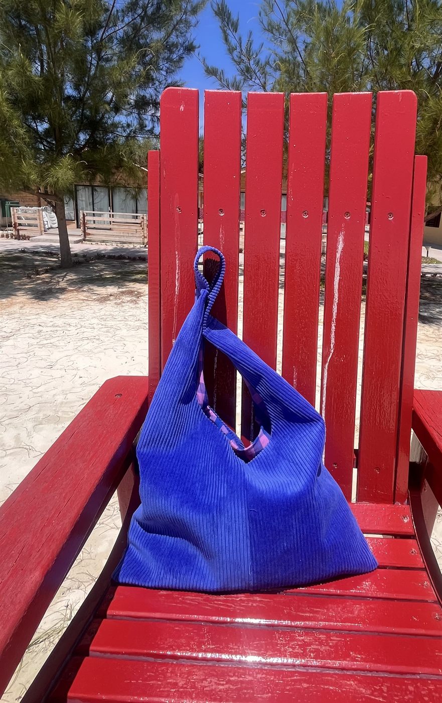 Sac cabas Kota en velours côtelé bleu roi, doublure rose, posé sur une chaise de plage rouge