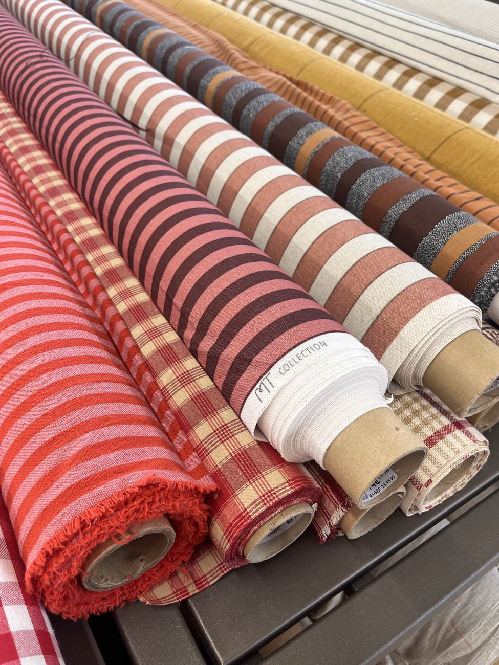 Rouleaux de tissus rayés et à carreaux dans des tons chauds, dans l'atelier